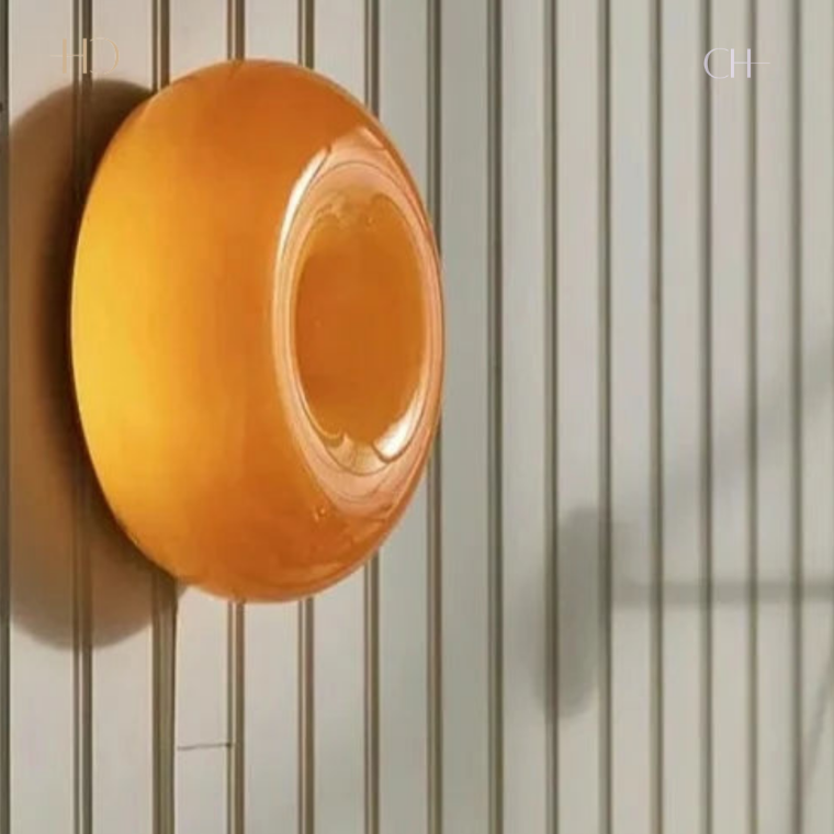 Bauhaus, a circular, donut-shaped, glass lamp. Featured in orange, pictured hung on a wall.