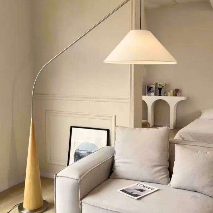 Ellis, a modern floor light, with a coned light brown base and a tapered golden arching arm, featured in a lightly decorated living room.