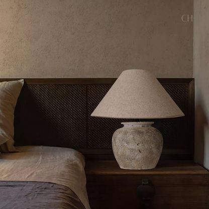 Kaia, a beige toned ceramic table lamp, pictured on a wooden bedside desk.