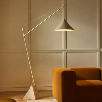 Quentin, a sculptural and minimalist floor light with a beige hued iron body, and a triangular marble base. Pictured in a room decorated with a burnt orange sofa.