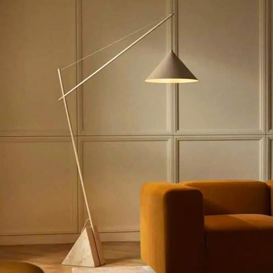 Quentin, a sculptural and minimalist floor light with a beige hued iron body, and a triangular marble base. Pictured in a room decorated with a burnt orange sofa.