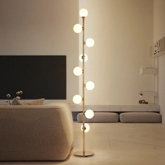 Atlas, a modern floor lamp, in brushed gold, with 9 circular bulbs in a minimalist styled room.