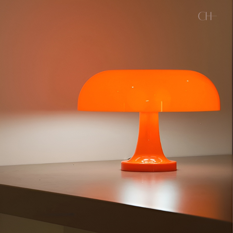 Giancarlo, an artistic, modern orange table lamp with a silhouette resembling a mushroom, pictured on a bare desk.