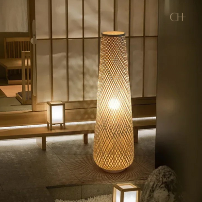 Solace, a cylindrical wicker floor lamp, pictured in Japanese styled interior featuring wooden benches and accent lamps.