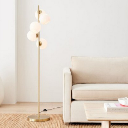 Galileo, a modern floor lamp with a gold-colored iron body and frosted glass bulbs, in a living room setting with a sofa and coffee table.