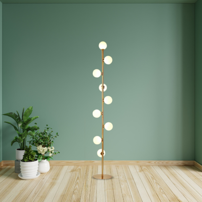 Atlas, a modern floor lamp, in brushed gold, with 9 circular bulbs spread the height of the lamp, placed in a bare, studio styled room.
