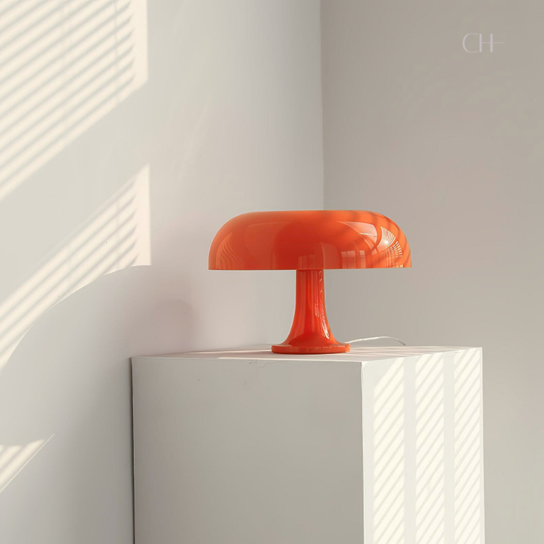 Giancarlo, a modern and artistic orange table lamp with a silhouette resembling a mushroom, placed on a white pedestal.