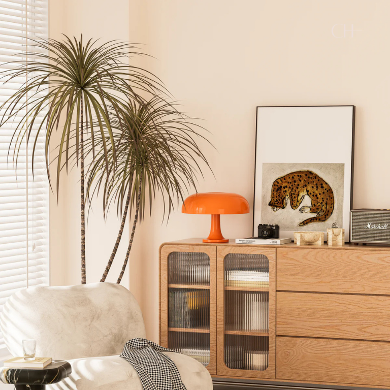 An artistically decorated living, featuring Giancarlo, a modern orange table lamp with a silhouette resembling a mushroom, pictured on  dresser next to a cheetah painting and a house plant.